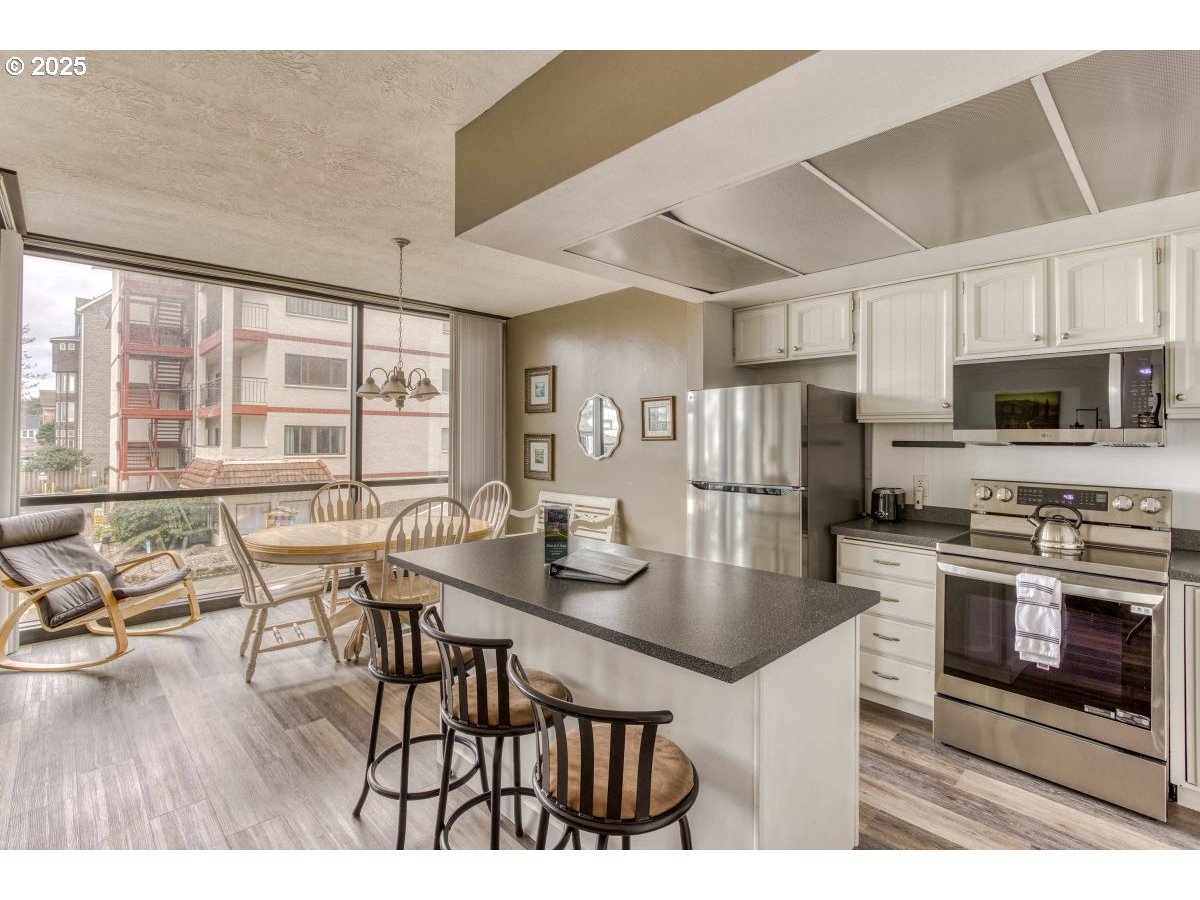 475 South Promenade, Unit 112 Seaside, OR 97138 - Photo 10 of 32 a kitchen with stainless steel appliances granite countertop a stove top oven a refrigerator a dining table and chairs with wooden floor