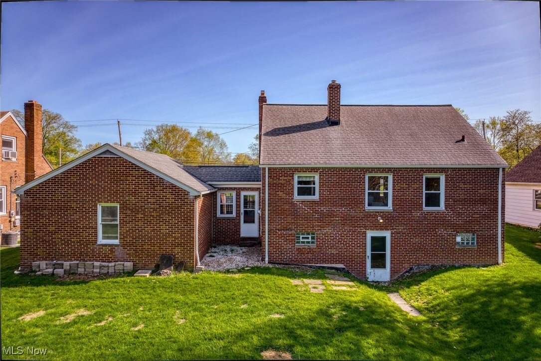 6315 Brookside Road Independence, OH 44131 - Photo 32 of 41 Rear view of property featuring brick siding, a shingled roof, a lawn, and a chimney