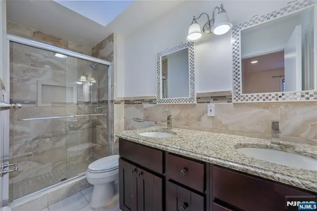 a bathroom with a granite countertop sink a toilet a mirror and shower