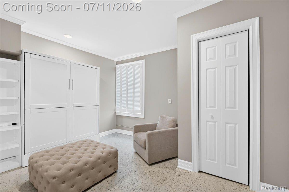 23750 East River Road Grosse Ile, MI 48138 - Photo 15 of 54 Room featuring a built-in white wall unit with cabinet doors, white bi-fold closet doors, crown molding, and a window with white louvered blinds