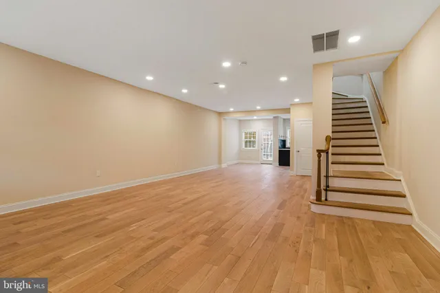 a view of empty room with wooden floor and kitchen