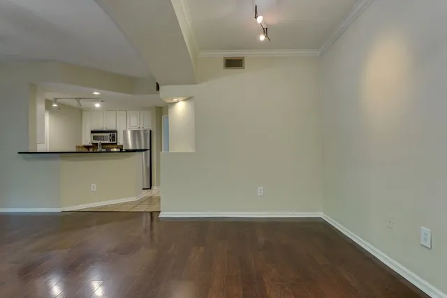 an empty room with wooden floor and kitchen view