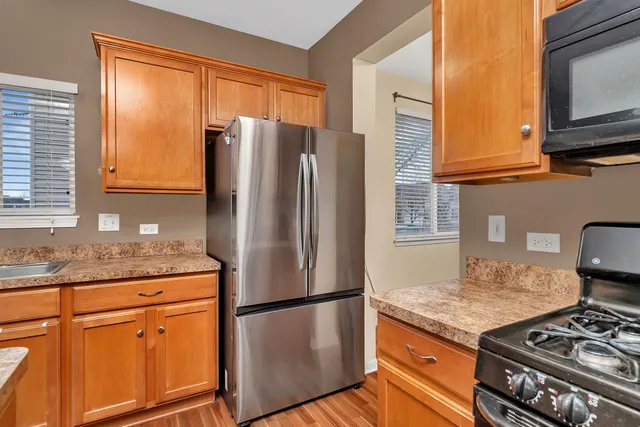 a kitchen with stainless steel appliances granite countertop a refrigerator a stove top oven a dining table and chairs with wooden floor