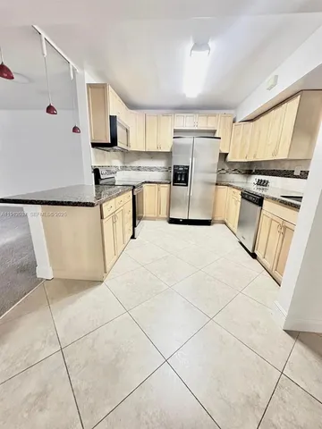 a kitchen with granite countertop a refrigerator and white cabinets