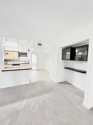 a view of an empty room with kitchen and window