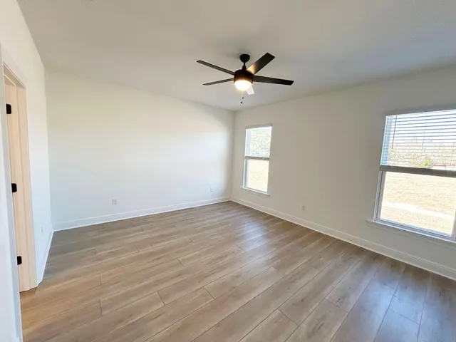 an empty room with wooden floor fan and windows