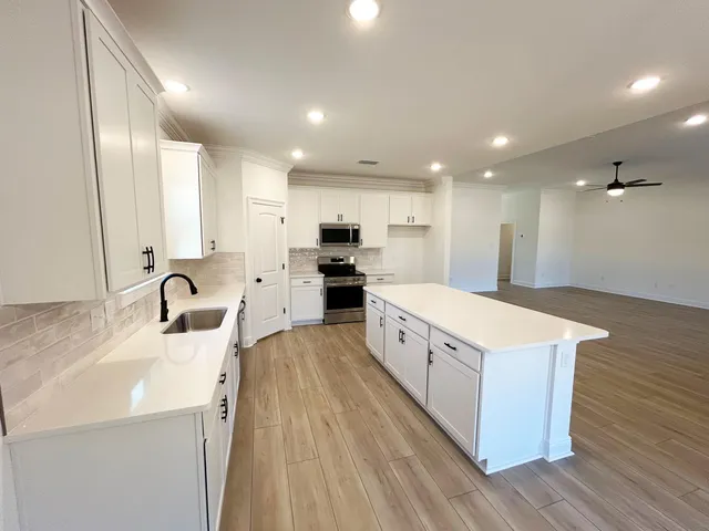 a large kitchen with stainless steel appliances a large counter top a stove a sink dishwasher and a refrigerator with wooden floor