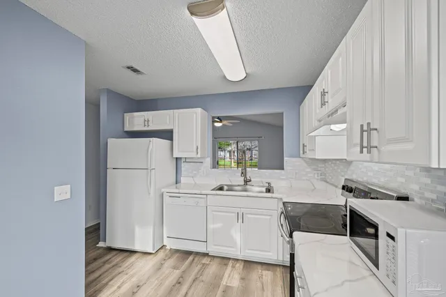 a kitchen with a sink a stove a refrigerator and white cabinets