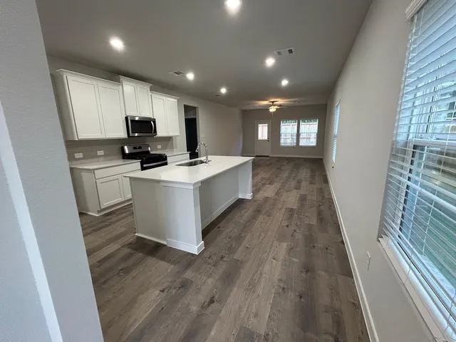 a kitchen with stainless steel appliances a sink a stove a refrigerator cabinets and a wooden floor