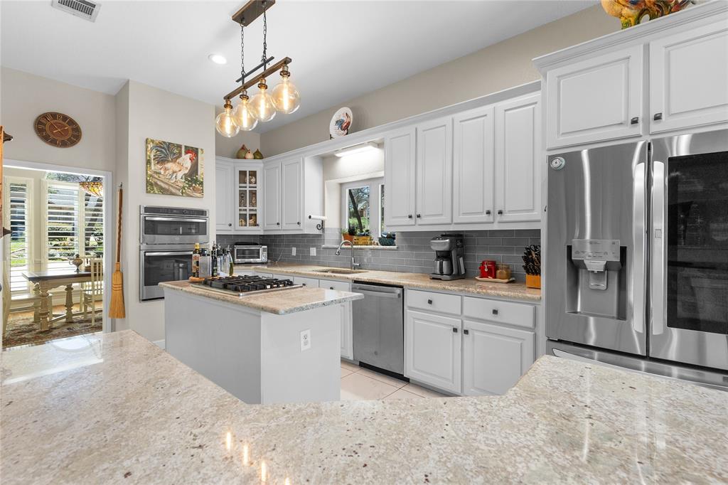 1007 Santa Fe Street Denton, TX 76205 - Photo 12 of 37 Kitchen with stainless steel appliances, white cabinetry, glass insert cabinets, light stone countertops, and a kitchen island
