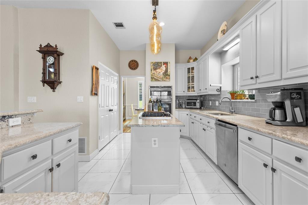 1007 Santa Fe Street Denton, TX 76205 - Photo 10 of 37 Kitchen with a center island, white cabinetry, glass insert cabinets, decorative backsplash, and light stone counters