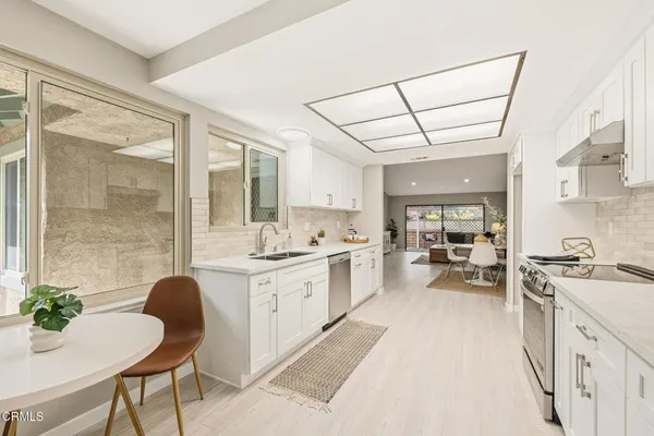 a open kitchen with stainless steel appliances granite countertop a stove a sink dishwasher and white cabinets with wooden floor