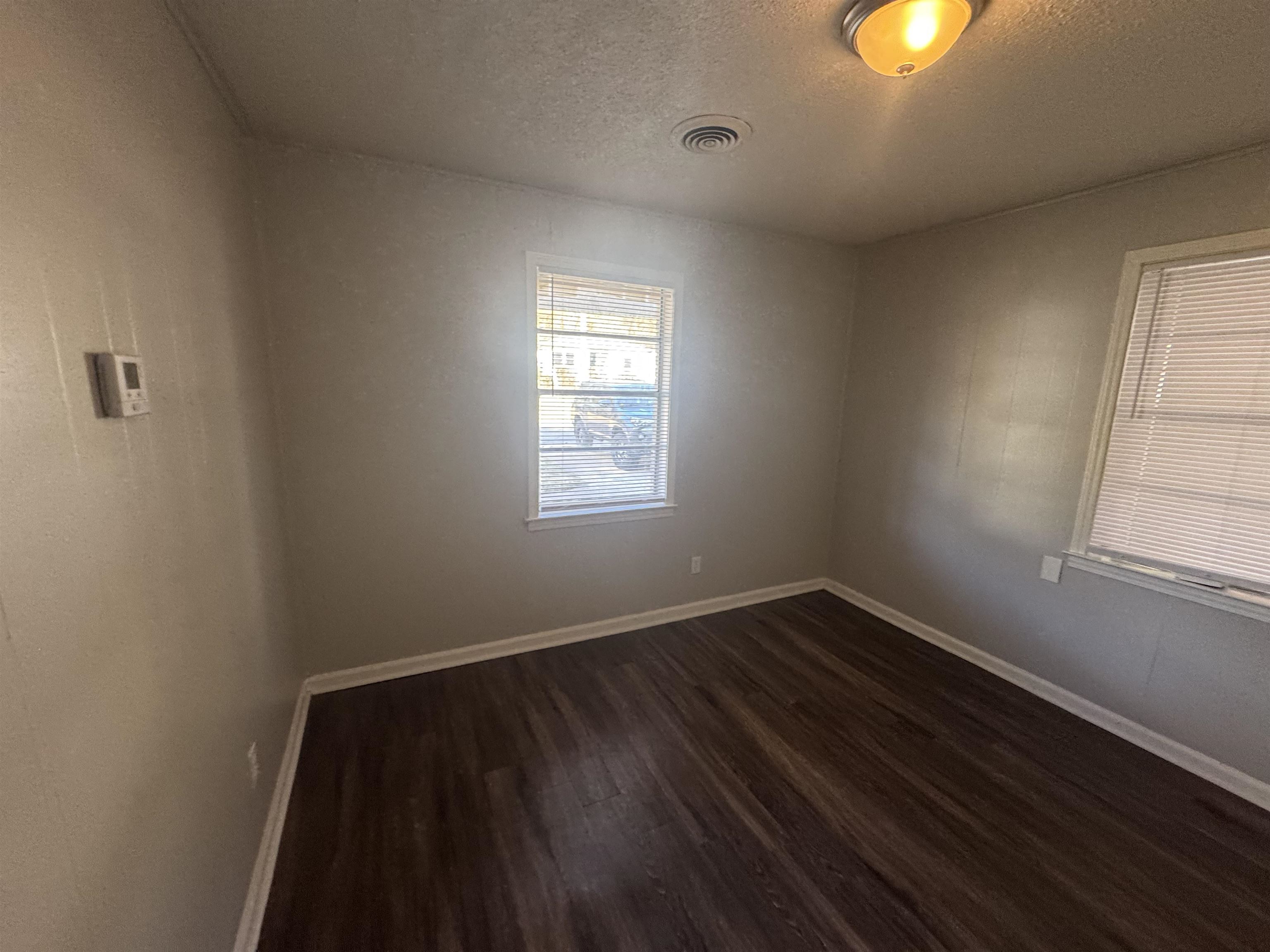 745 Harahan Road Memphis, TN 38109 - Photo 8 of 12 Wood-finish flooring, two windows with blinds, ceiling-mounted light fixture, and wall-mounted thermostat