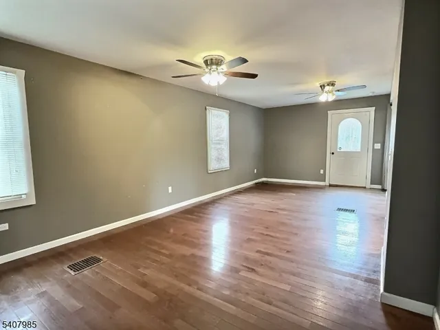 an empty room with wooden floor chandelier fan and windows
