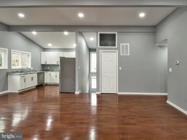 a view of an empty room with wooden floor and a kitchen