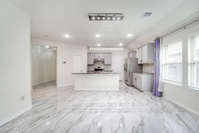 a view of kitchen with stainless steel appliances granite countertop a refrigerator a sink dishwasher a stove and white cabinets with wooden floor