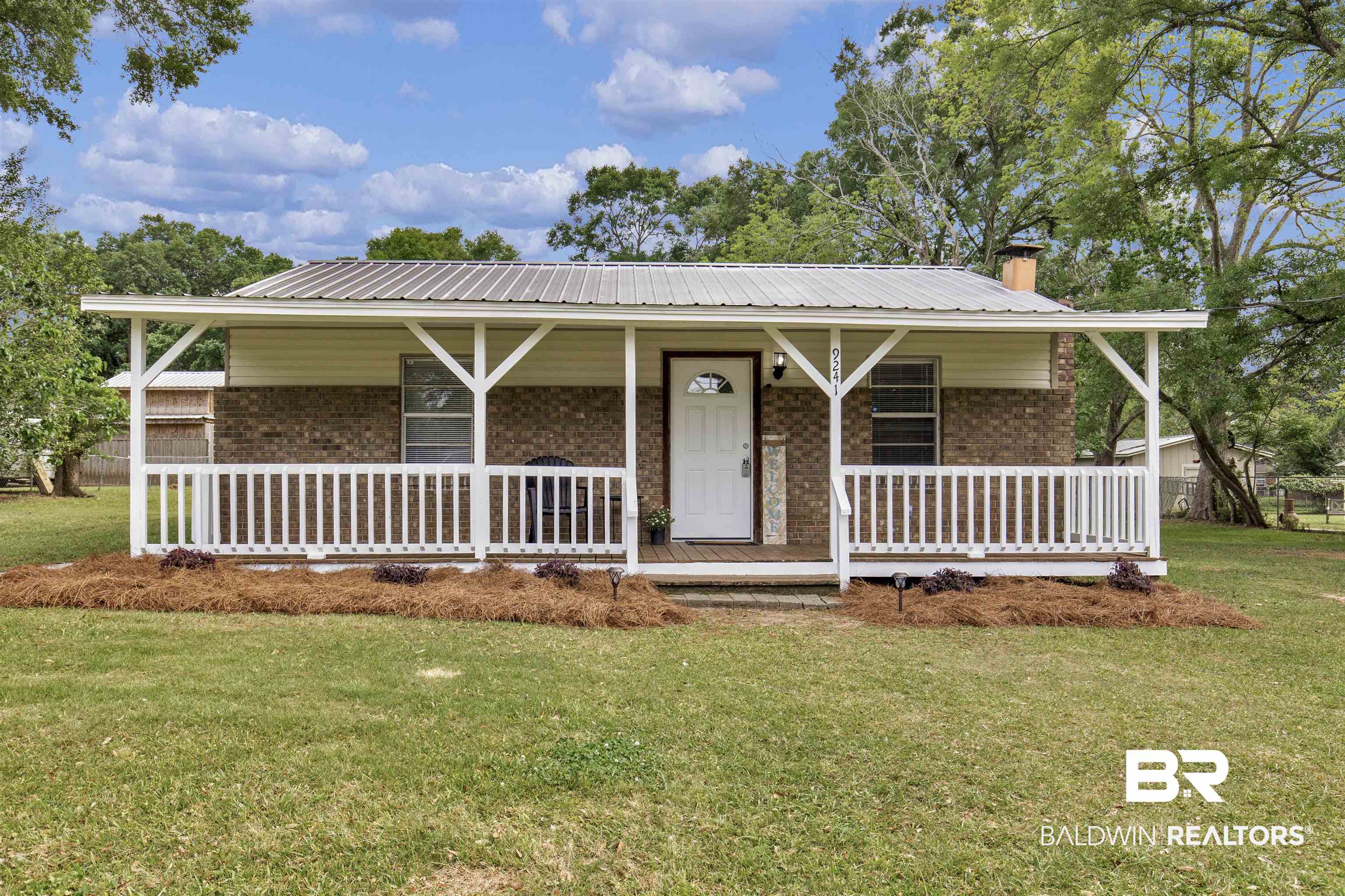 View of front facade featuring brick siding, a porch, metal roof, and a front yard