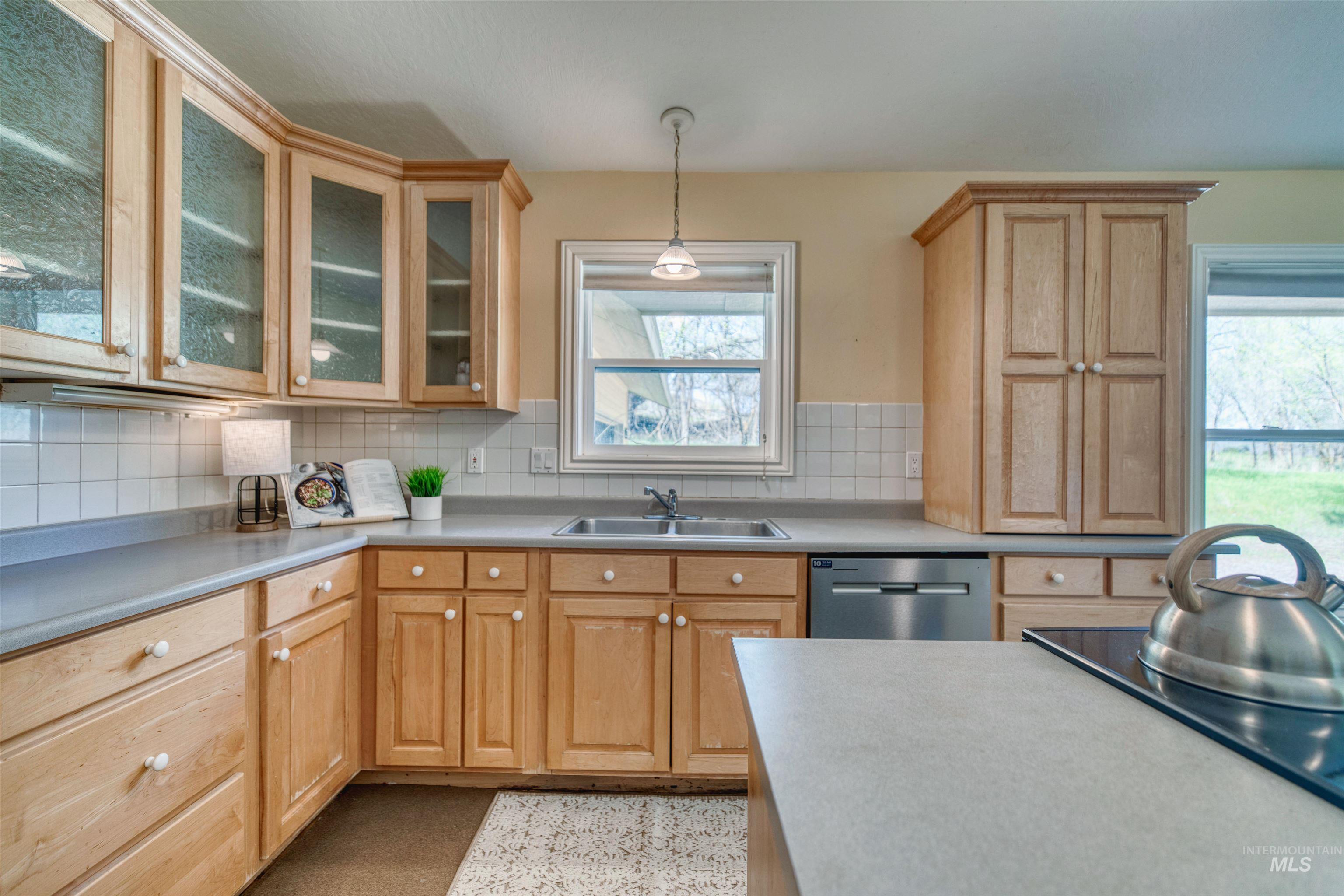 1295 15th Street Vale, OR 97918 - Photo 11 of 50 Kitchen featuring hanging light fixtures, light countertops, stainless steel dishwasher, glass insert cabinets, and decorative backsplash