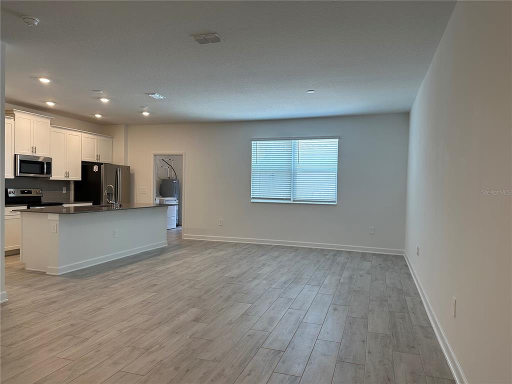 3128 Addison Boulevard St. Cloud, FL 34771 - Photo 3 of 35 an empty room with wooden floor and kitchen view