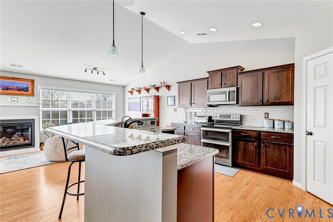 7401 Leaf Fall Way Mechanicsville, VA 23111 - Photo 13 of 48 a kitchen with stainless steel appliances granite countertop a stove top oven a sink dishwasher a dining table and chairs with wooden floor