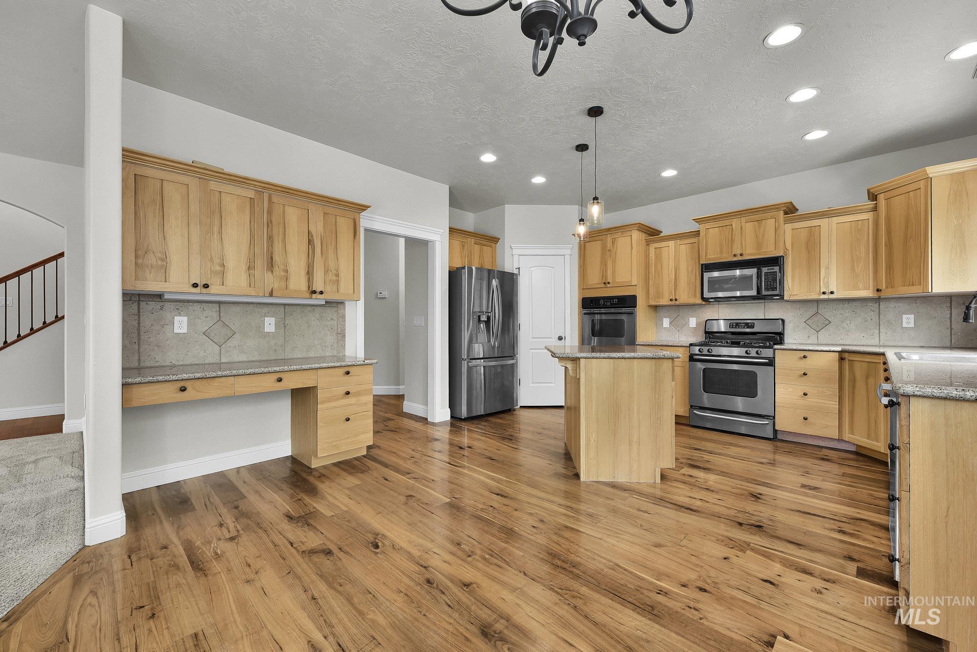 2172 West Cedar Grove Street Meridian, ID 83646 - Photo 10 of 49 Open-concept kitchen featuring wood-finish flooring, light wood cabinetry, stainless steel appliances, granite countertops, and a central island with pendant lighting