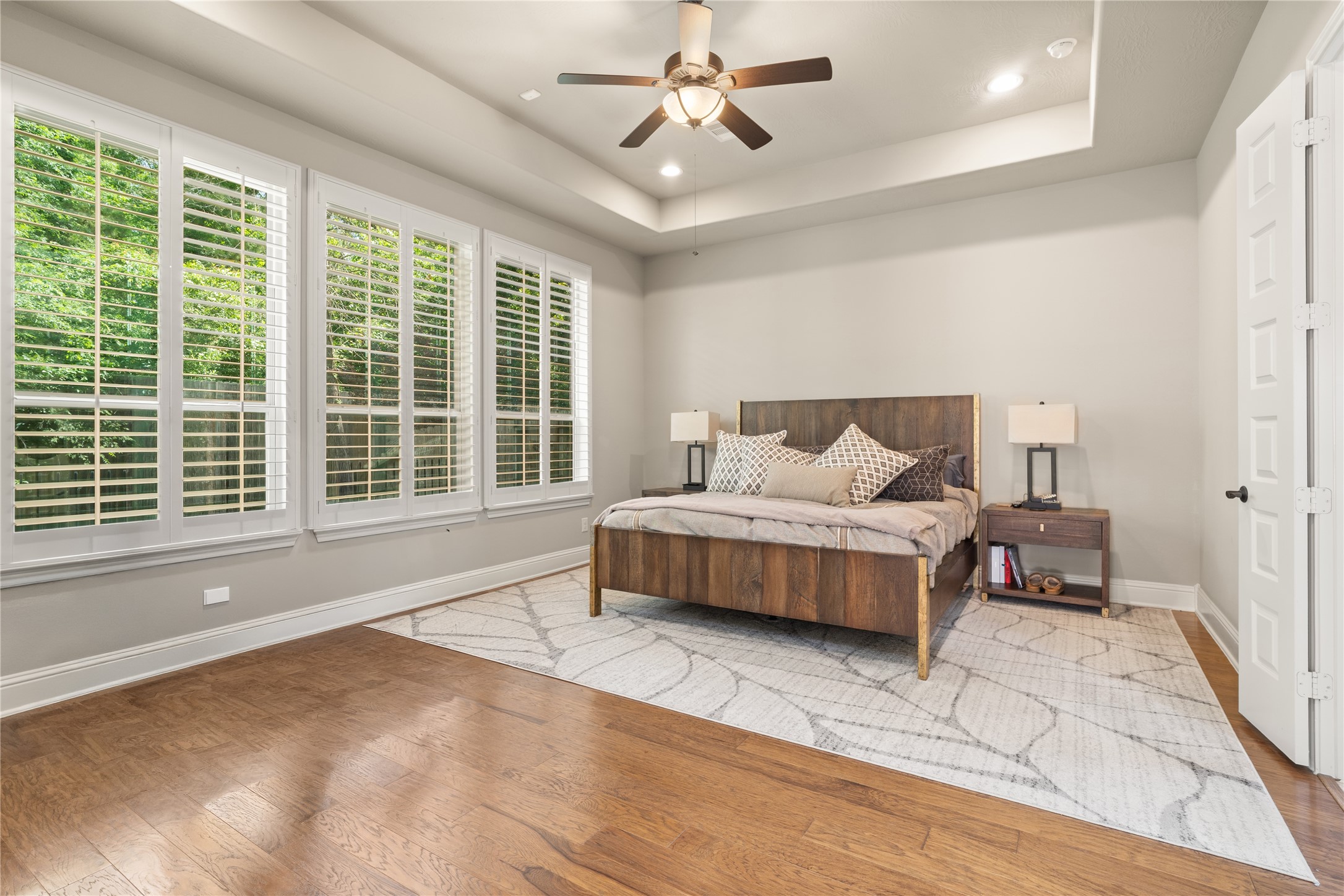 19813 Cullen Ridge Drive Porter, TX 77365 - Photo 20 of 44 Experience the serenity of this spacious primary bedroom, boasting abundant natural light through elegant shuttered windows, warm hardwood floors, and a stylish ceiling fan for ultimate comfort.