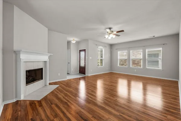 a view of an empty room with wooden floor fireplace and a window