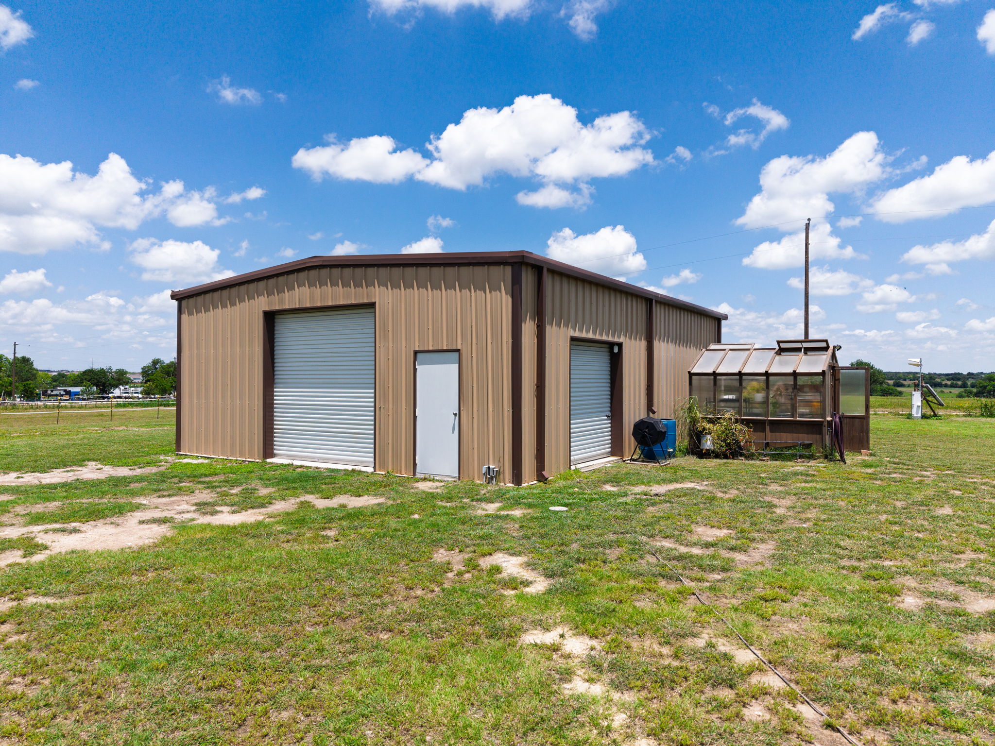 120 Rae Lane Jarrell, TX 76537 - Photo 16 of 40 Two-bay metal outbuilding featuring two roll-up garage doors, a pedestrian entry door, and an attached greenhouse