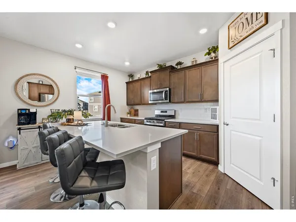 a living room with stainless steel appliances kitchen island granite countertop a stove a sink a refrigerator and a dining table with wooden floor