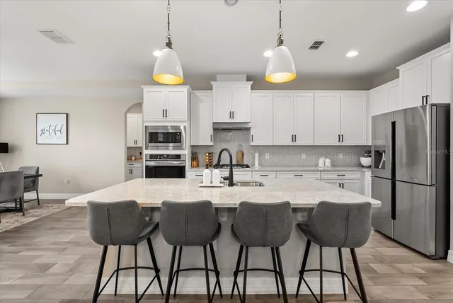 a kitchen with stainless steel appliances kitchen island granite countertop a stove a sink a refrigerator and white cabinets with wooden floor