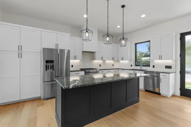 a kitchen with stainless steel appliances granite countertop a refrigerator a sink dishwasher a stove and white cabinets with wooden floor