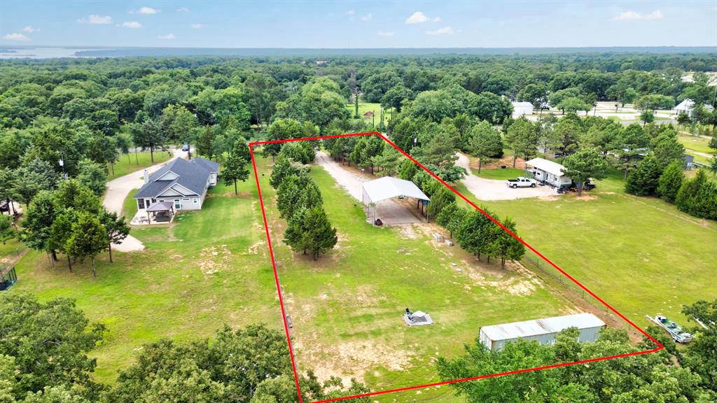 1469 Cedar Mills Road Gordonville, TX 76245 - Photo 10 of 12 Expansive grassy lot featuring mature trees, a detached carport structure, a long gravel driveway, and a distant water body