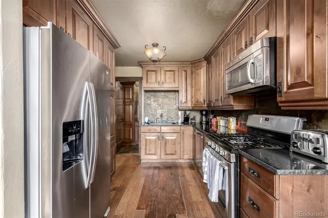 a kitchen with stainless steel appliances granite countertop a refrigerator a stove and a sink with wooden floor