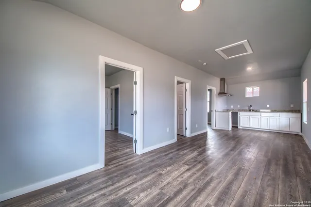 a view of an empty room and kitchen with wooden floor