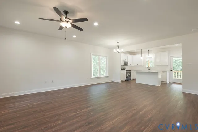 a view of an empty room with wooden floor and a kitchen