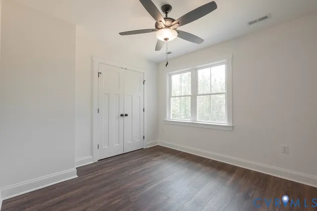 an empty room with wooden floor chandelier fan and windows