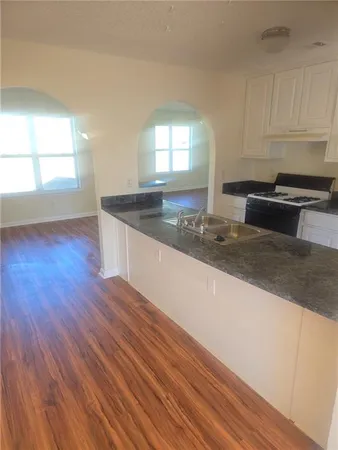 a kitchen with granite countertop a stove a sink and white cabinets with wooden floor