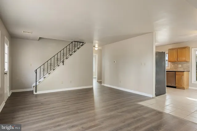 a view of empty room with wooden floor and kitchen