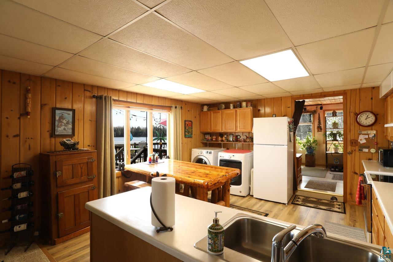1198 West Mink Road Cotton, MN 55724 - Photo 5 of 23 Kitchen with freestanding refrigerator, wood walls, wall chimney range hood, washer and clothes dryer, and light countertops