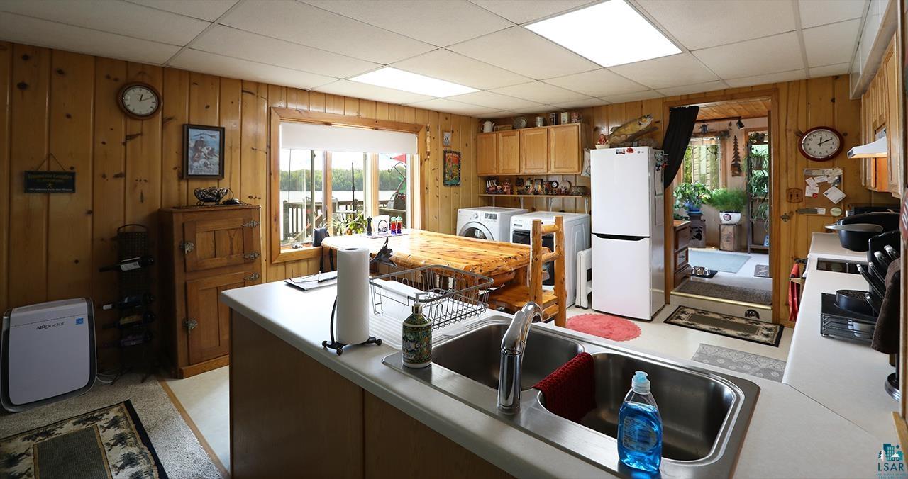 1198 West Mink Road Cotton, MN 55724 - Photo 5 of 23 Kitchen with freestanding refrigerator, wood walls, wall chimney range hood, washer and clothes dryer, and light countertops