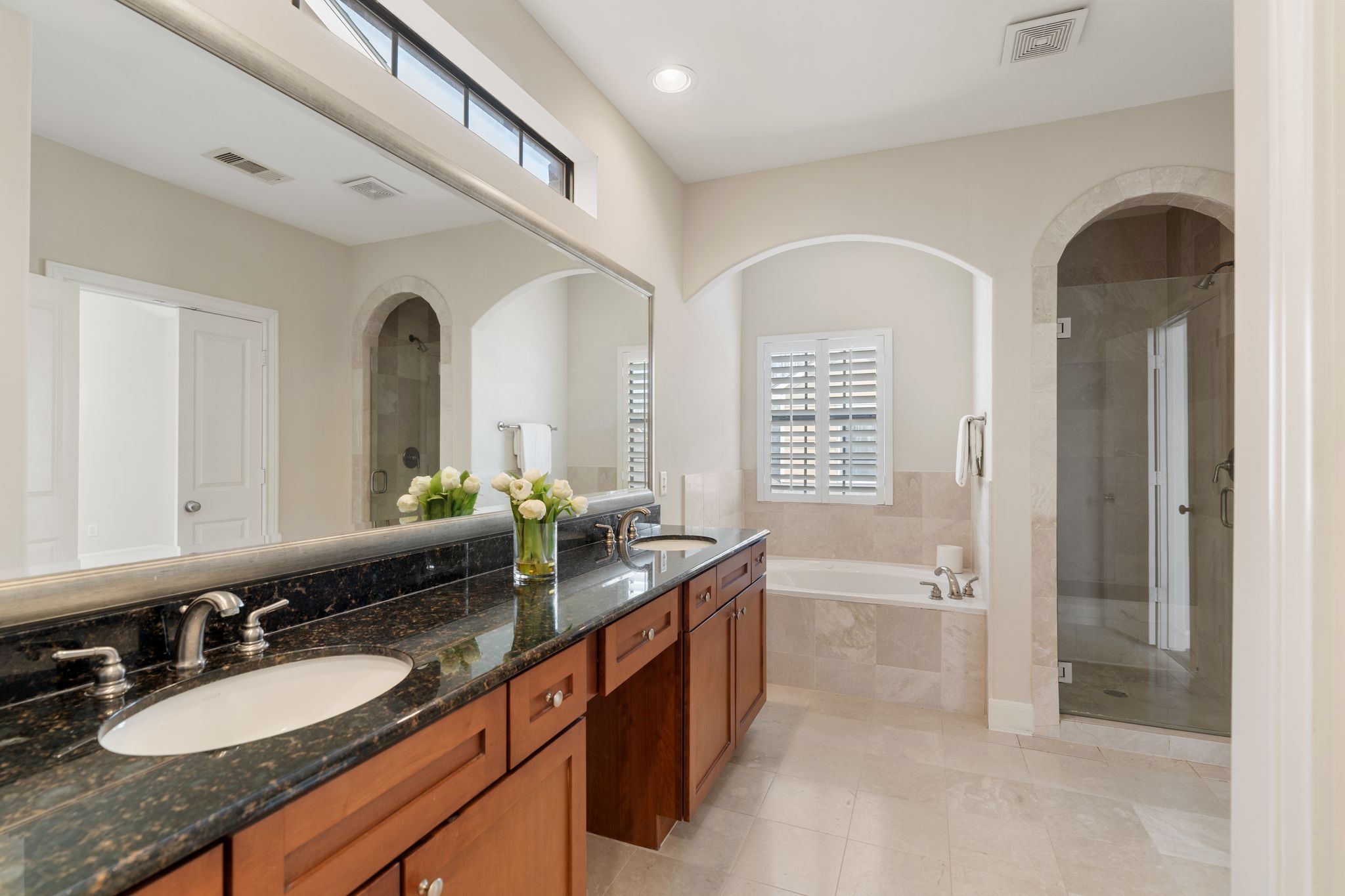 121 Roy Street Houston, TX 77007 - Photo 18 of 29 Spacious primary bath features a double vanity with granite countertops, beautiful mirror, and wood cabinets. Spa bathtub, a separate glass-enclosed shower, and bright lighting, creating a luxurious and functional space.
