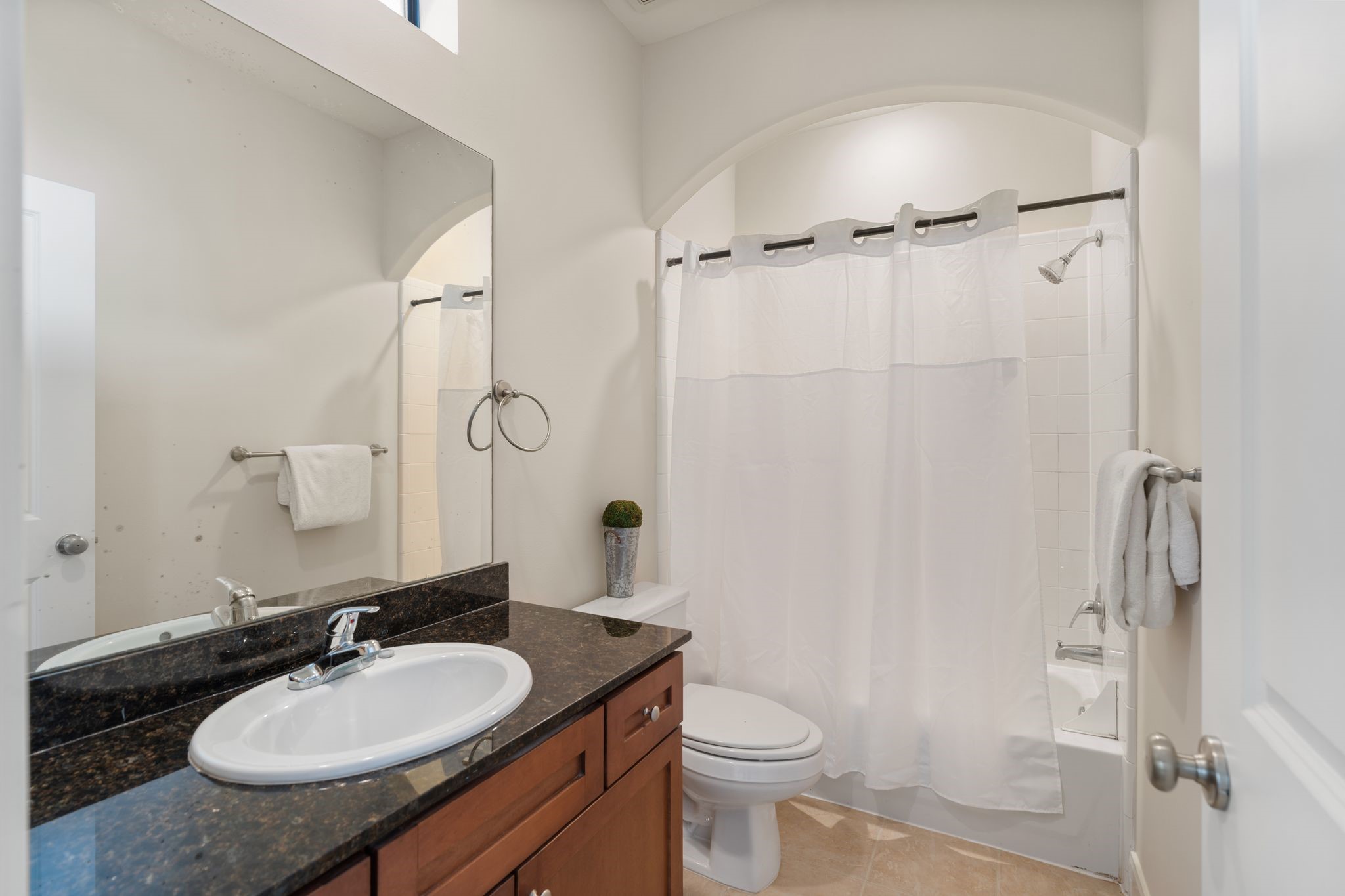 121 Roy Street Houston, TX 77007 - Photo 23 of 29 This is a well-lit bathroom featuring a modern vanity with a granite countertop and sink, a shower-tub combo with neutral tile flooring.