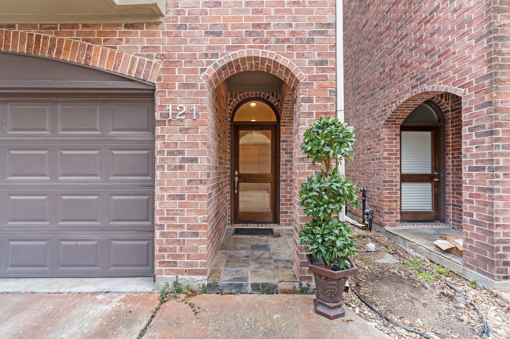 121 Roy Street Houston, TX 77007 - Photo 24 of 29 This photo shows the brick townhouse entrance with an arched doorway, a glass front door. The 2 car garage door is adjacent. This side space between the townhomes adds extra natural light in the interior.