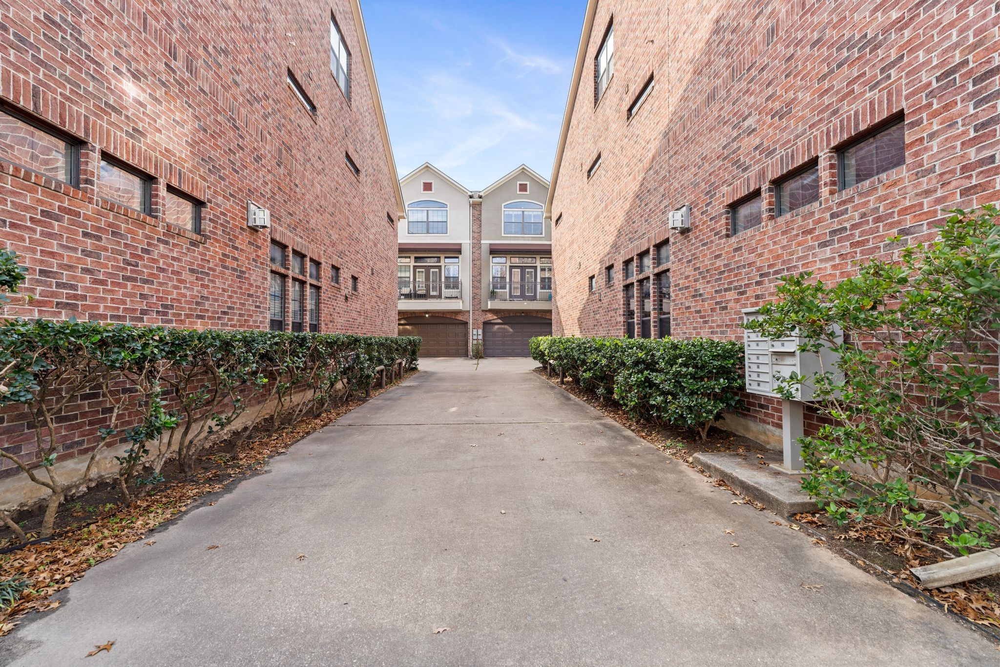 121 Roy Street Houston, TX 77007 - Photo 25 of 29 This photo shows the paved driveway entrance to community flanked by red brick townhouses with hedges along the sides. The setting is clean and well-maintained, offering a sense of privacy and community.