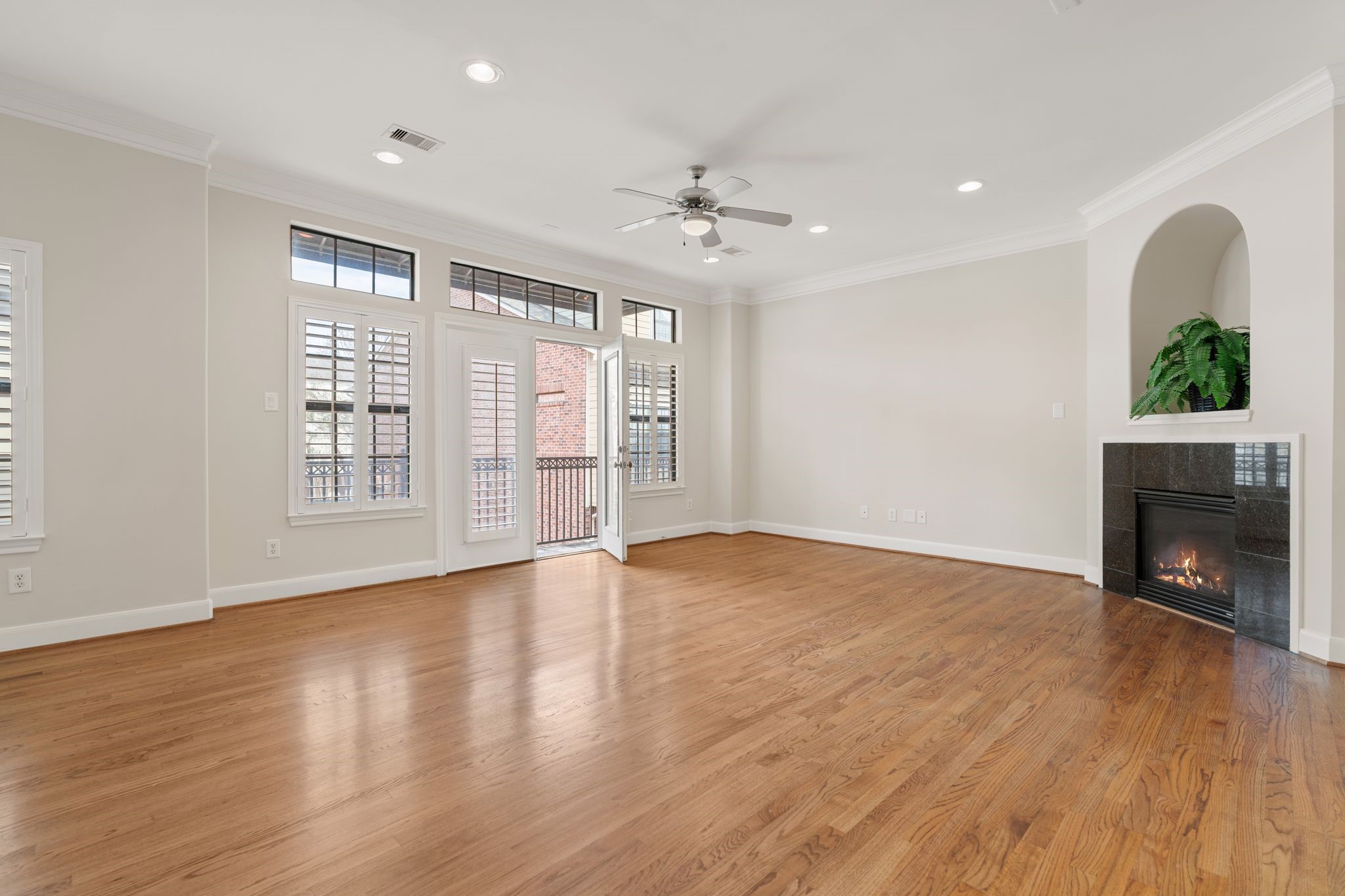 121 Roy Street Houston, TX 77007 - Photo 3 of 29 Bright and spacious living room with hardwood floors, a cozy fireplace, and large windows featuring plantation shutters. Double doors leading to a covered balcony patio.