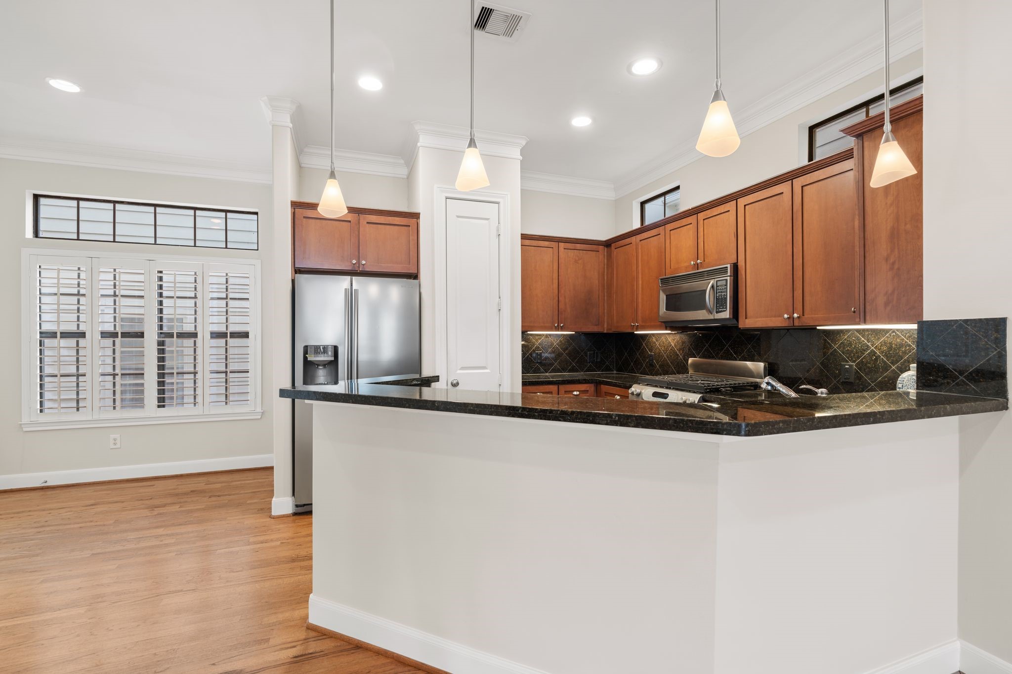 121 Roy Street Houston, TX 77007 - Photo 10 of 29 The kitchen with warm wood cabinetry, stainless steel appliances, and a sleek black granite countertop. The space is well-lit with pendant and recessed lighting, and features a breakfast bar with room for seating. Windows with shutters add natural light and charm to the room and another seating area.
