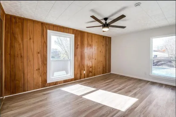 an empty room with wooden floor fan and windows