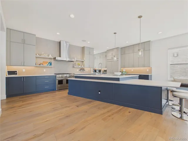 a kitchen with stainless steel appliances kitchen island granite countertop a stove a sink a refrigerator and white cabinets with wooden floor