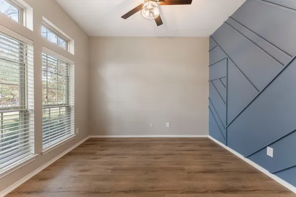 an empty room with wooden floor fan and windows