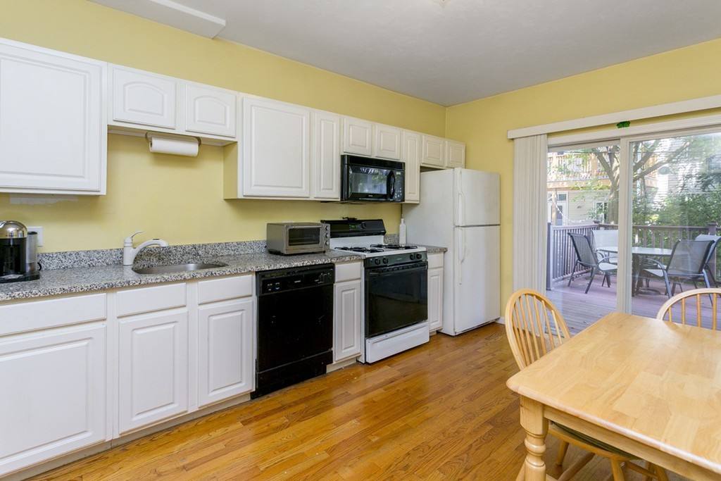 a kitchen with stainless steel appliances granite countertop a stove a sink dishwasher a refrigerator white cabinets and wooden floor next to a window